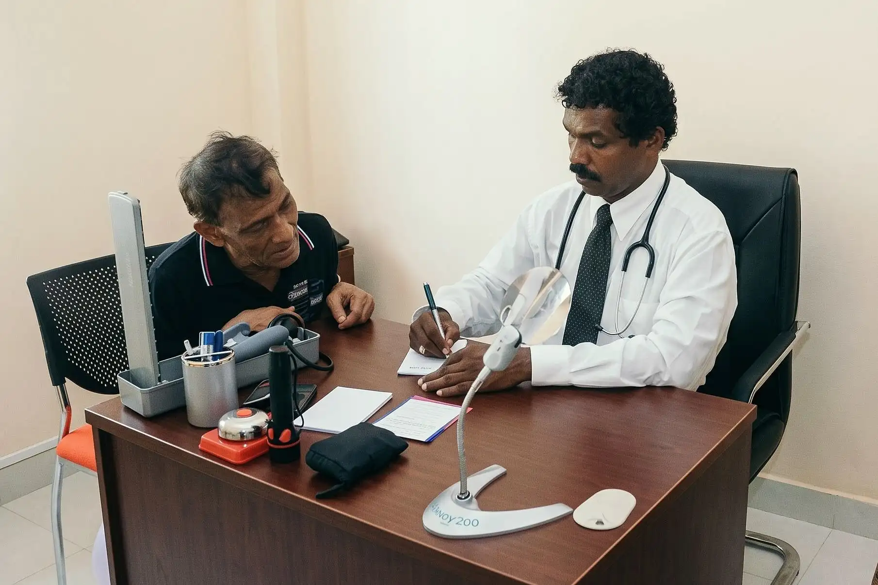 A doctor at the IMANA Medical Clinic writes up a consultation with a patient beside him